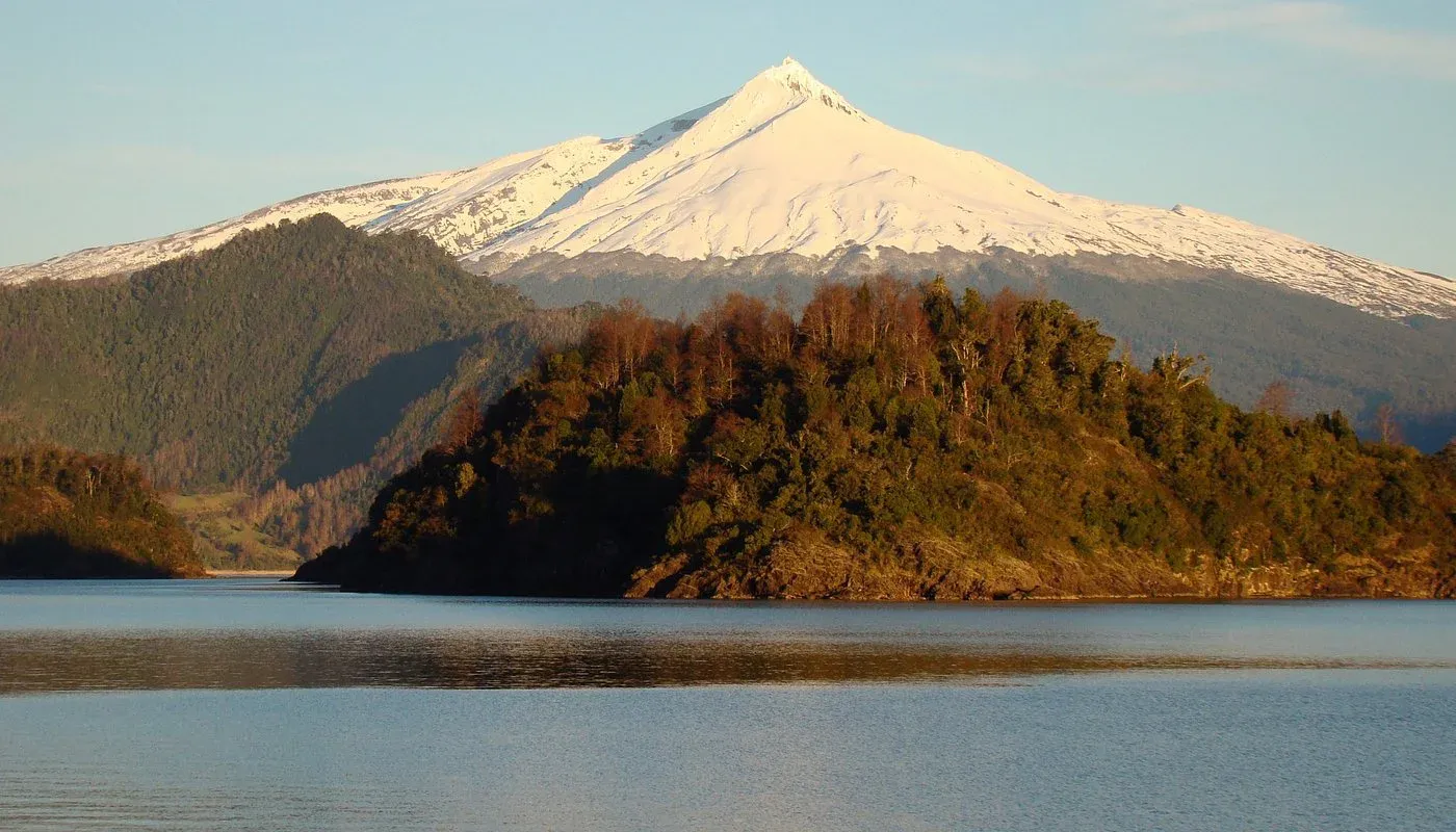 Volcán Mocho-Choshuenco reflejado en el lago Panguipulli con bosque nativo en la orilla